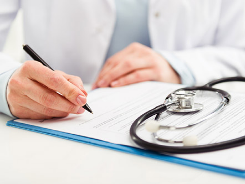 Ein Arzt unterzeichnet ein Formular auf dem ein Stethoskop liegt