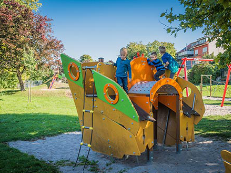 Kinder spielen auf einem bunten Spielplatzgerät in Form eines Schiffes