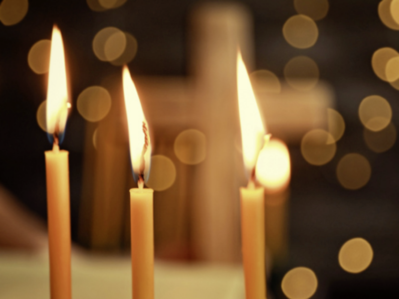 Drei brennende Kerzen vor einem dunklen Hintergrund