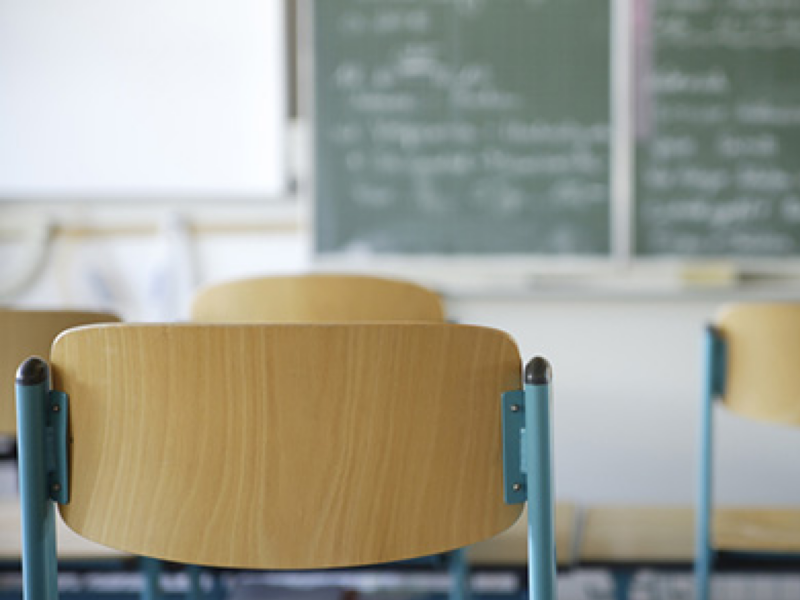 Der Stuhl in einem Klassenzimmr steht im Vordergrund einer Tafel