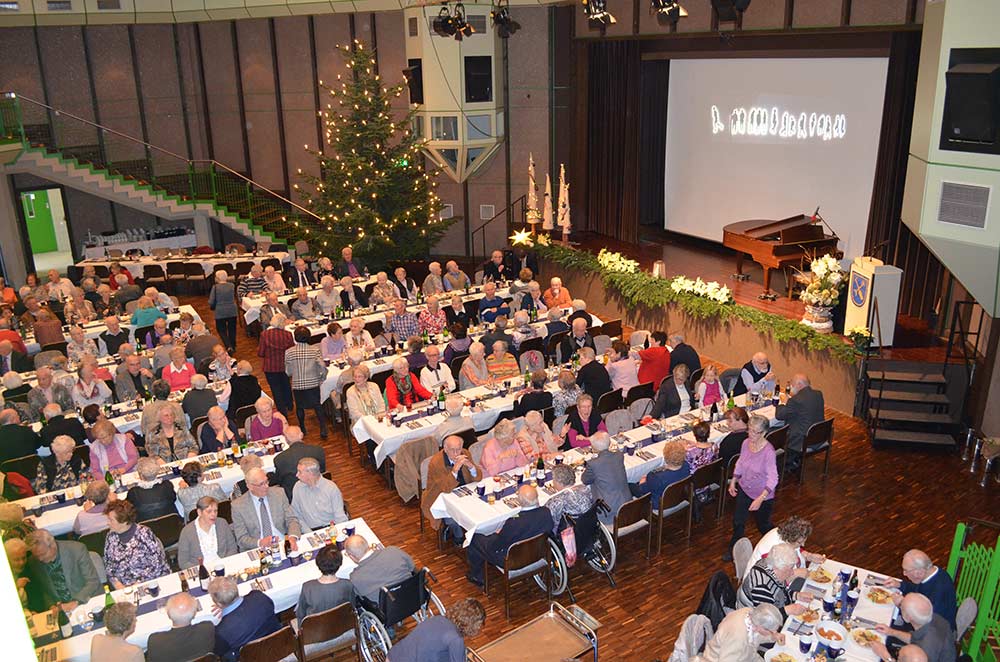 Senioren sitzen bei der Adventsfeier der Gemeinde an festlich weihnachtlich geschmückten Tischen